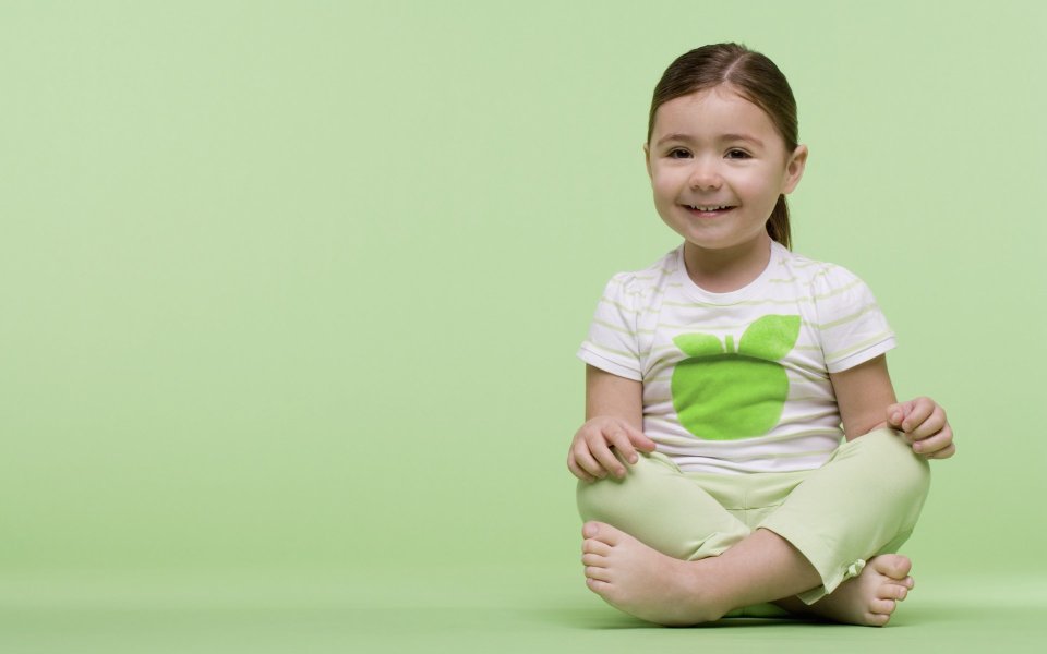 Cute Little Girl Sitting Cross Legged On Light Green Background