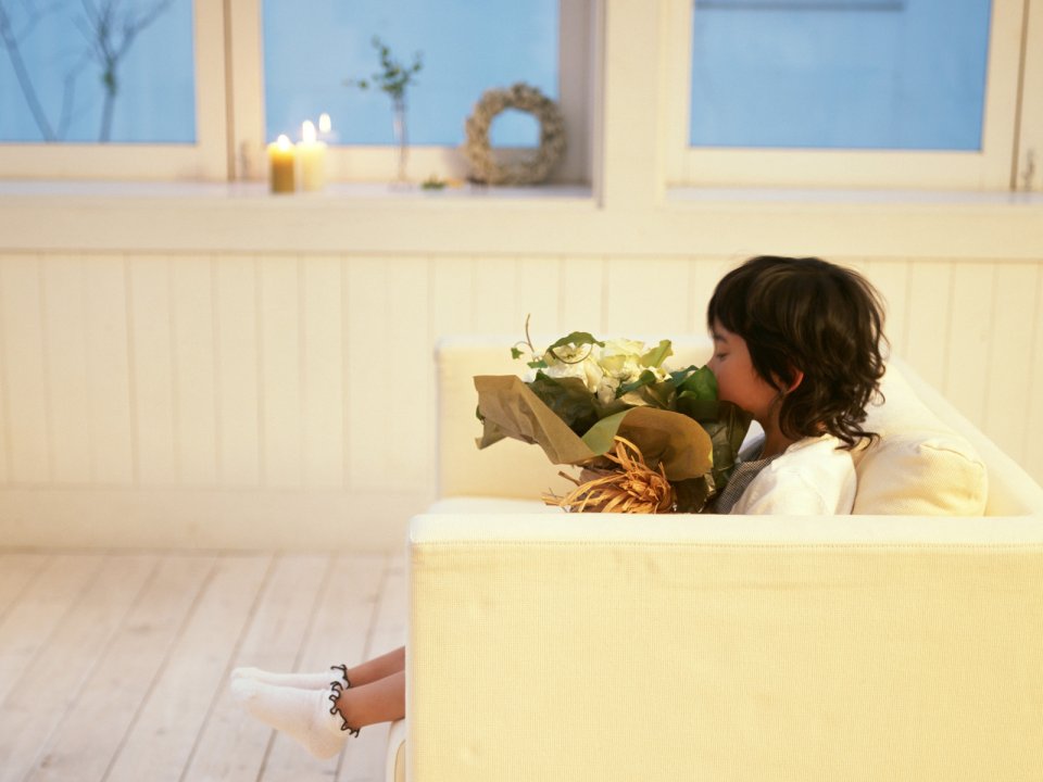 Little Girl Sitting On Sofa Smelling Flower Bouquet At Home