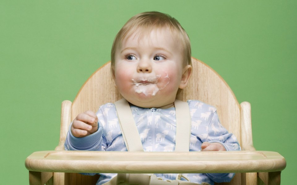 Cute Baby With Food Stains Sitting On Wooden High Chair