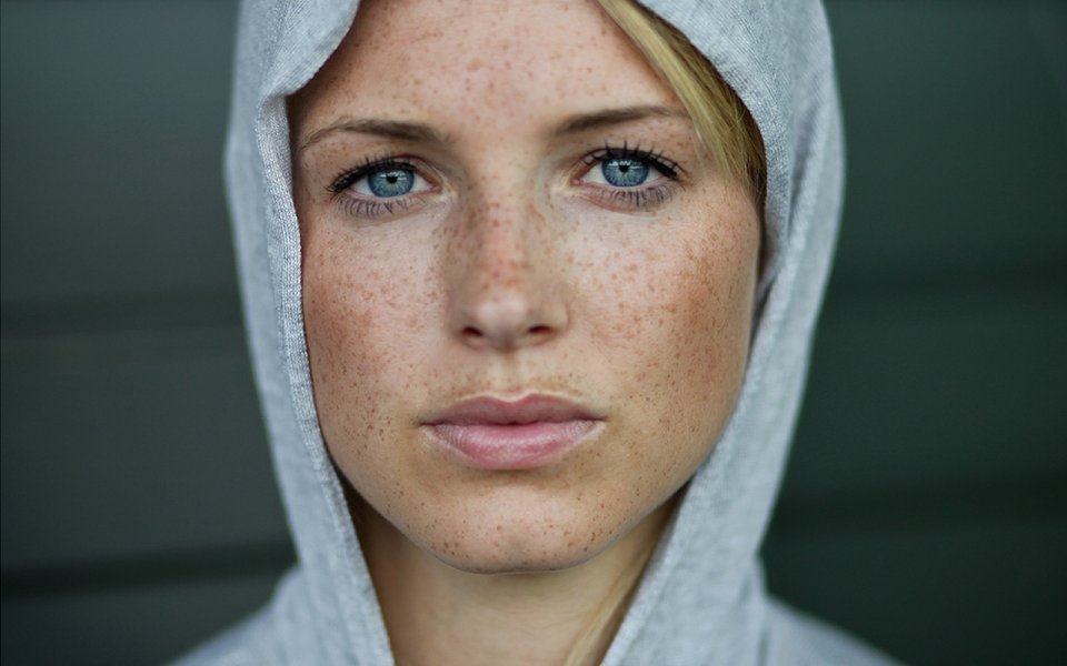 身着灰色连帽衫的雀斑蓝眼女性人像特写