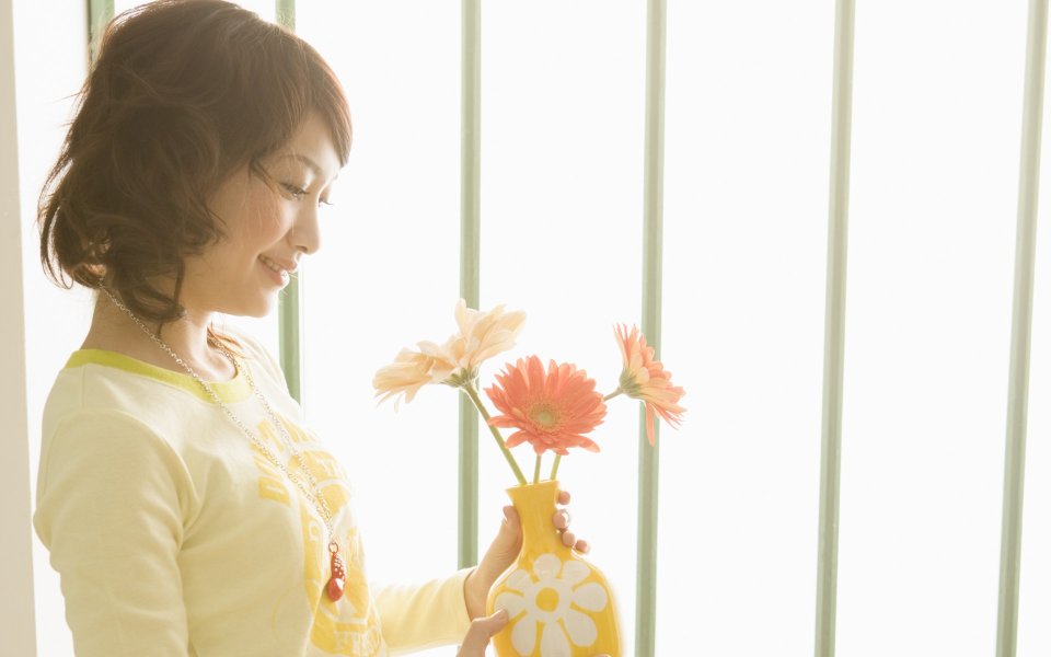 暖光窗边手持非洲菊花瓶的温柔居家女性