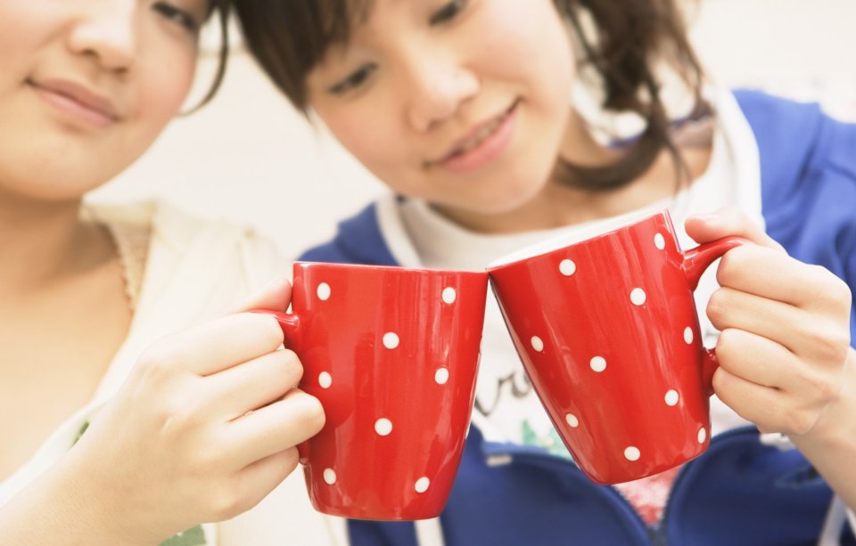 两位年轻女生居家持红色波点马克杯碰杯温馨日常