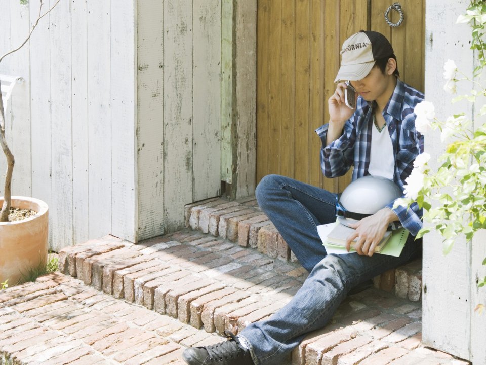 Young Man Sitting On Red Brick Porch Calling On Phone Sunny Day