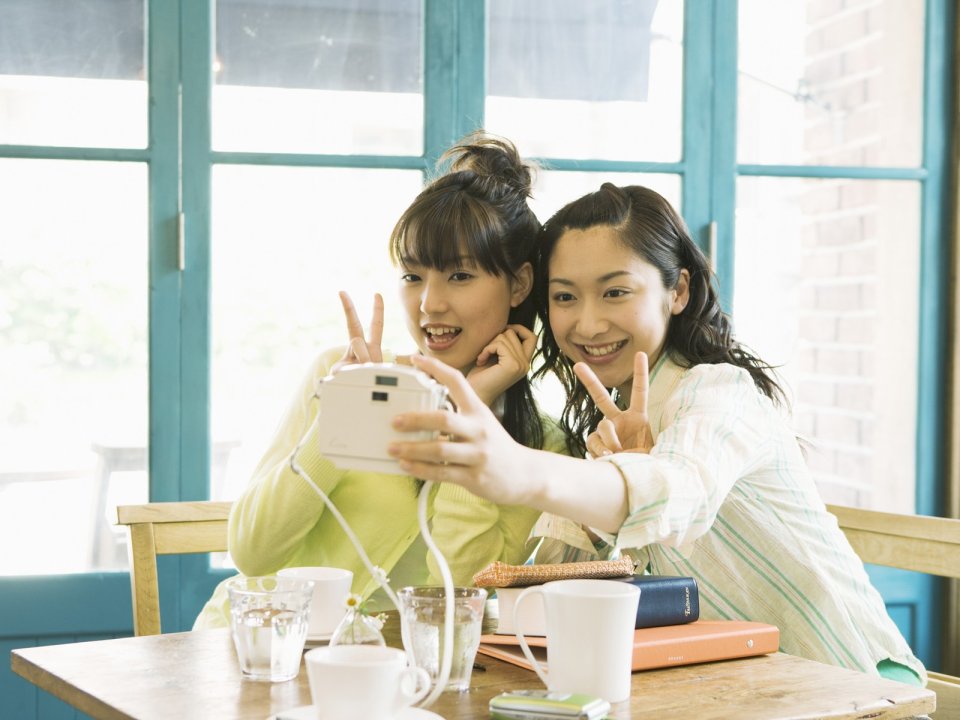 Two Girlfriends Taking Selfie With Instant Camera In Cafe