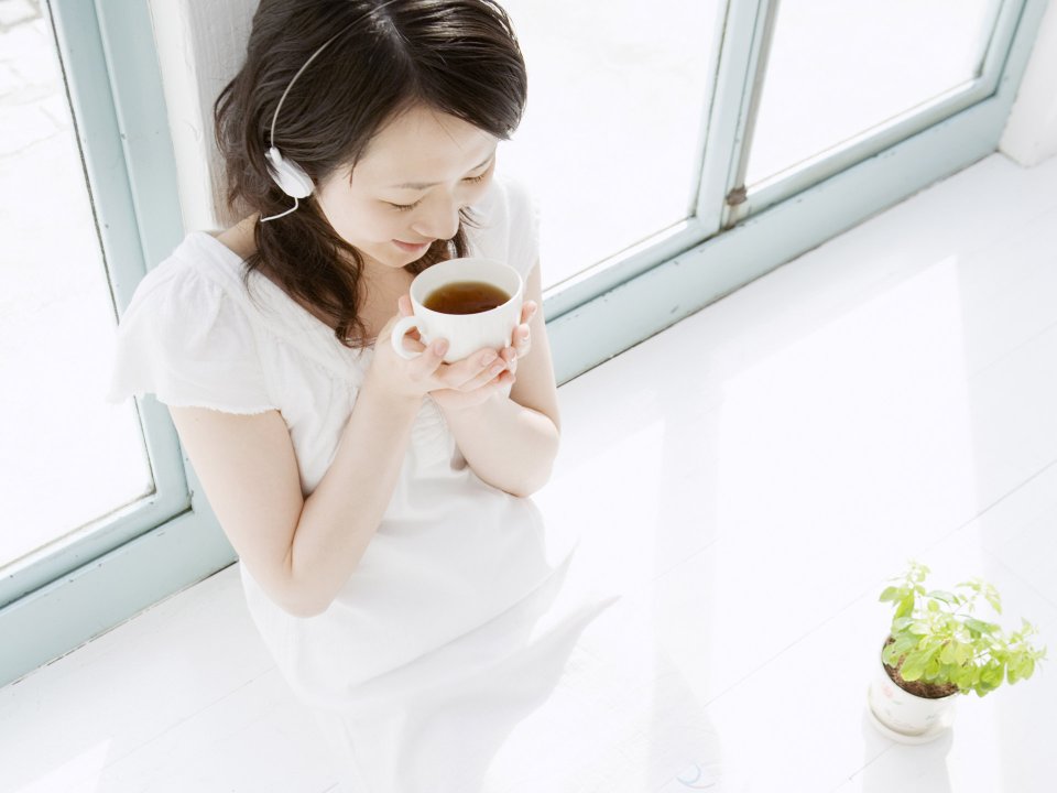 日系居家少女窗边手捧热茶戴耳机享受休闲时光