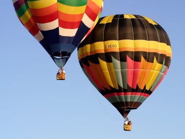 Two Colorful Manned Hot Air Balloons Flying Under Clear Blue Sky