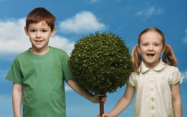 Two Little Children Hold Round Topiary Tree Blue Sky Background