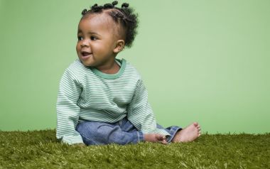 Cute Black Baby Sitting On Lawn With Green Background