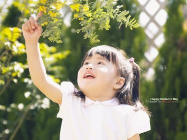 Cute Little Girl Touching Yellow Mimosa Flowers In Sunny Garden