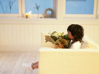 Little Girl Sitting On Sofa Smelling Flower Bouquet At Home