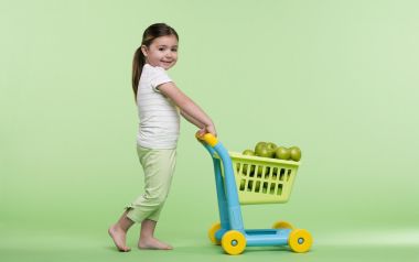 Little Girl Pushing Toy Shopping Cart Full Of Green Apples