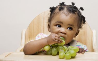 Cute Little Black Toddler Eating Green Grapes On Wooden High Chair