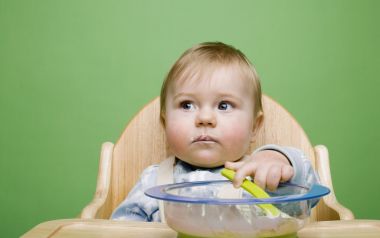 坐在实木餐椅上尝试自主进食的金发萌娃