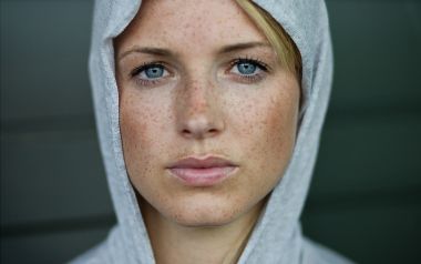 身着灰色连帽衫的雀斑蓝眼女性人像特写