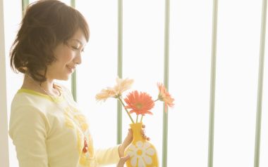 暖光窗边手持非洲菊花瓶的温柔居家女性