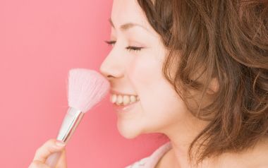 粉色背景前手持粉色腮红刷的甜美年轻女性美妆人像写真