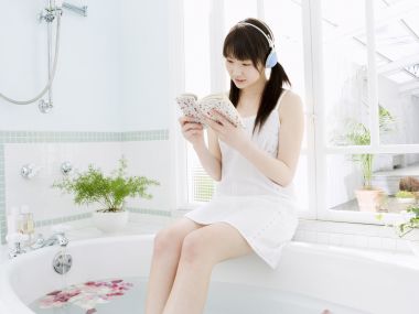 Relaxing Young Girl Reading With Headphone By Bright Bathroom Window