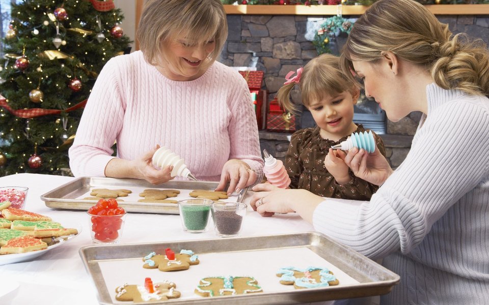Three Generation Family Decorating Gingerbread Cookies By Christmas Tree