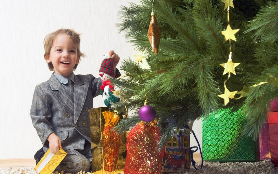 Little Boy In Suit Hanging Snowman Ornament On Christmas Tree