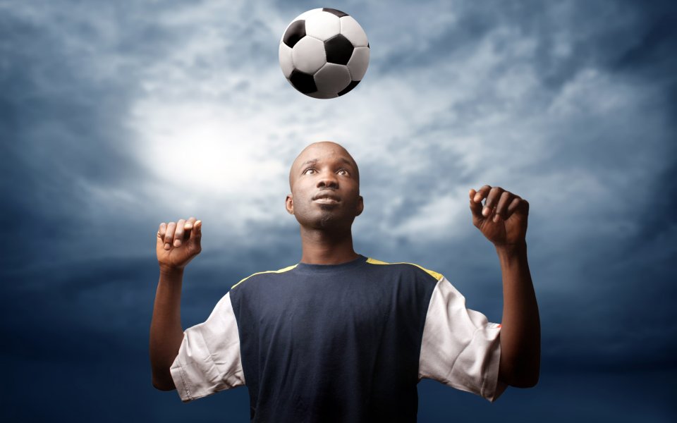 Black Soccer Player Juggling Ball Over Cloudy Sky