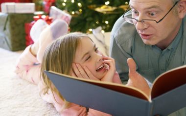 Father And Daughter Reading By Christmas Tree
