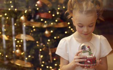 Little Girl Holding Snow Globe Before Christmas Tree