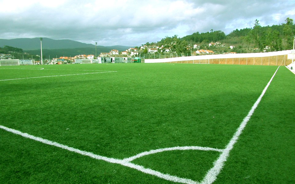 Artificial Turf Football Field Near Rural Village Under Cloudy Sky