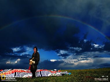中国高原草原 雨后彩虹下的藏族男子与经幡