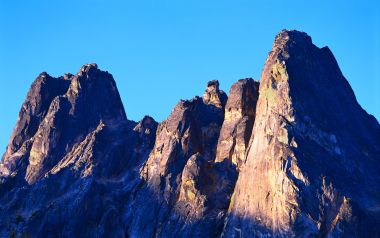 晴朗蓝天背景下晨光映照的陡峭花岗岩尖峰
